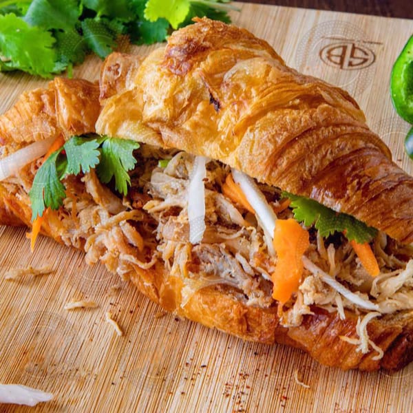 A Paris Banh Mi croissant sandwich filled with meat, pickled carrots, daikon, and cilantro.