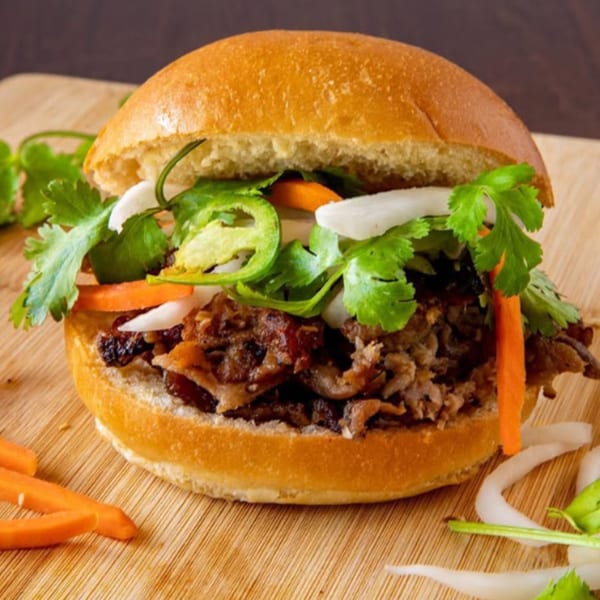 A Vietnamese banh mi sandwich with meat, cilantro, carrots, onions, and jalapeños on a wooden board.