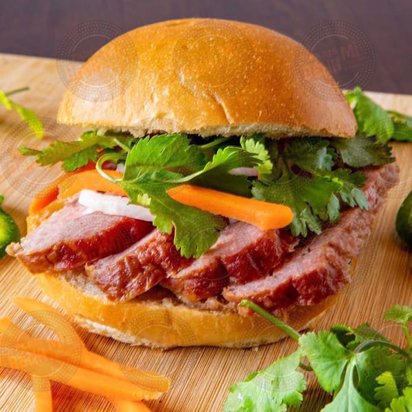A Vietnamese banh mi sandwich with sliced meat, carrots, and cilantro on a wooden board.