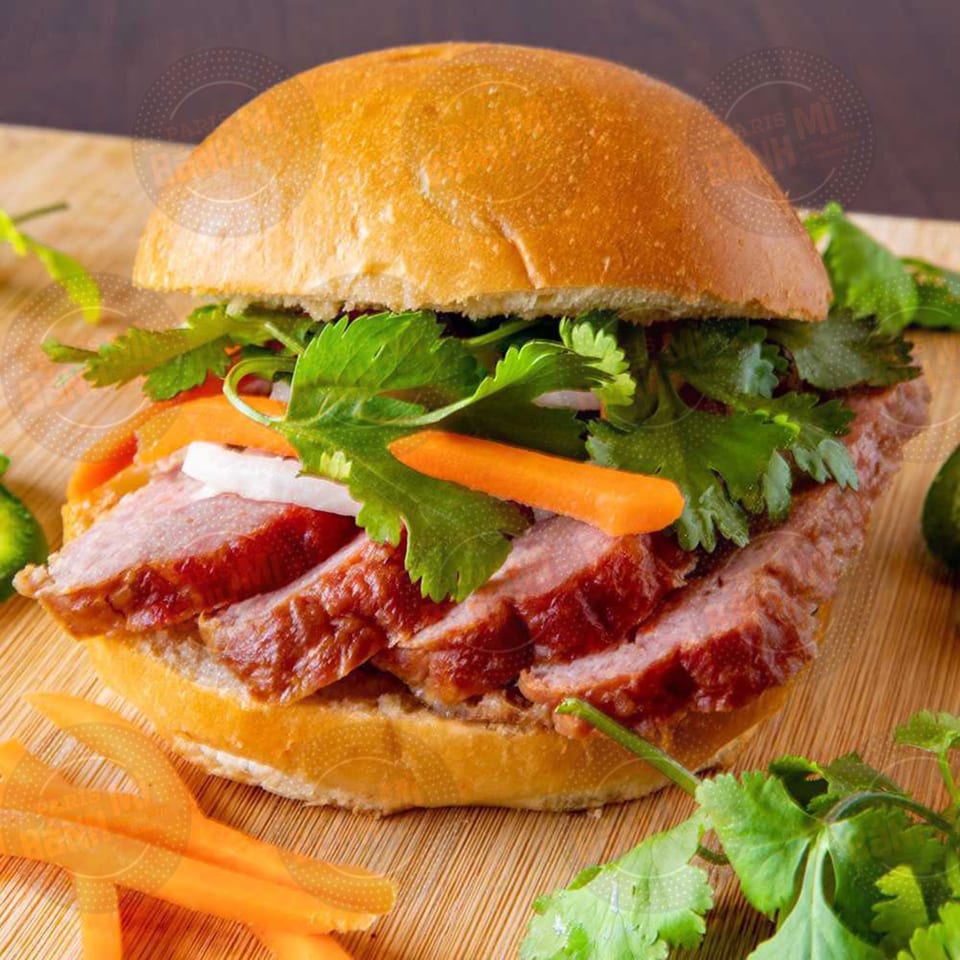 A Vietnamese banh mi sandwich with sliced meat, carrots, and cilantro on a wooden board.