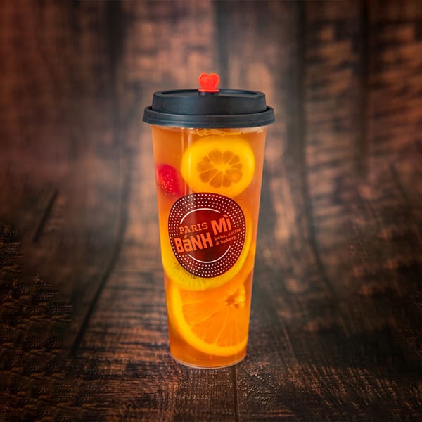 Paris Banh Mi fruit tea with orange, kiwi, and strawberry slices on a wooden table.